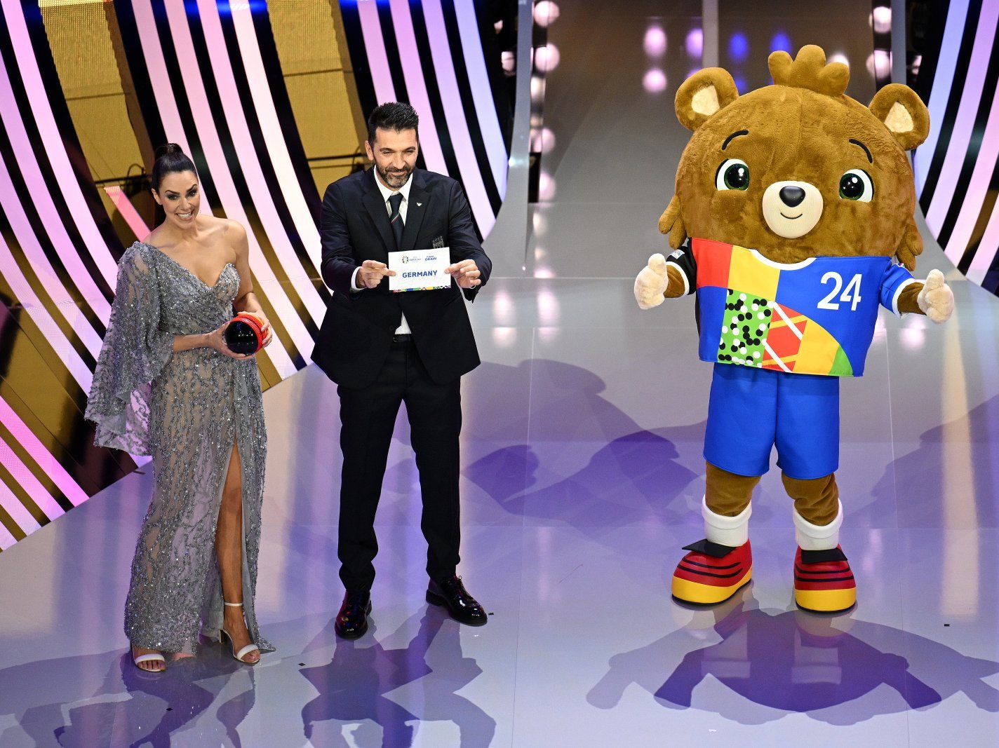 Gianluigi Buffon zeigt eine weiße Karte mit Germany drauf, links neben ihm steht Moderatorin Esther Sedlaczek und rechts Albärt, das Maskottchen 
